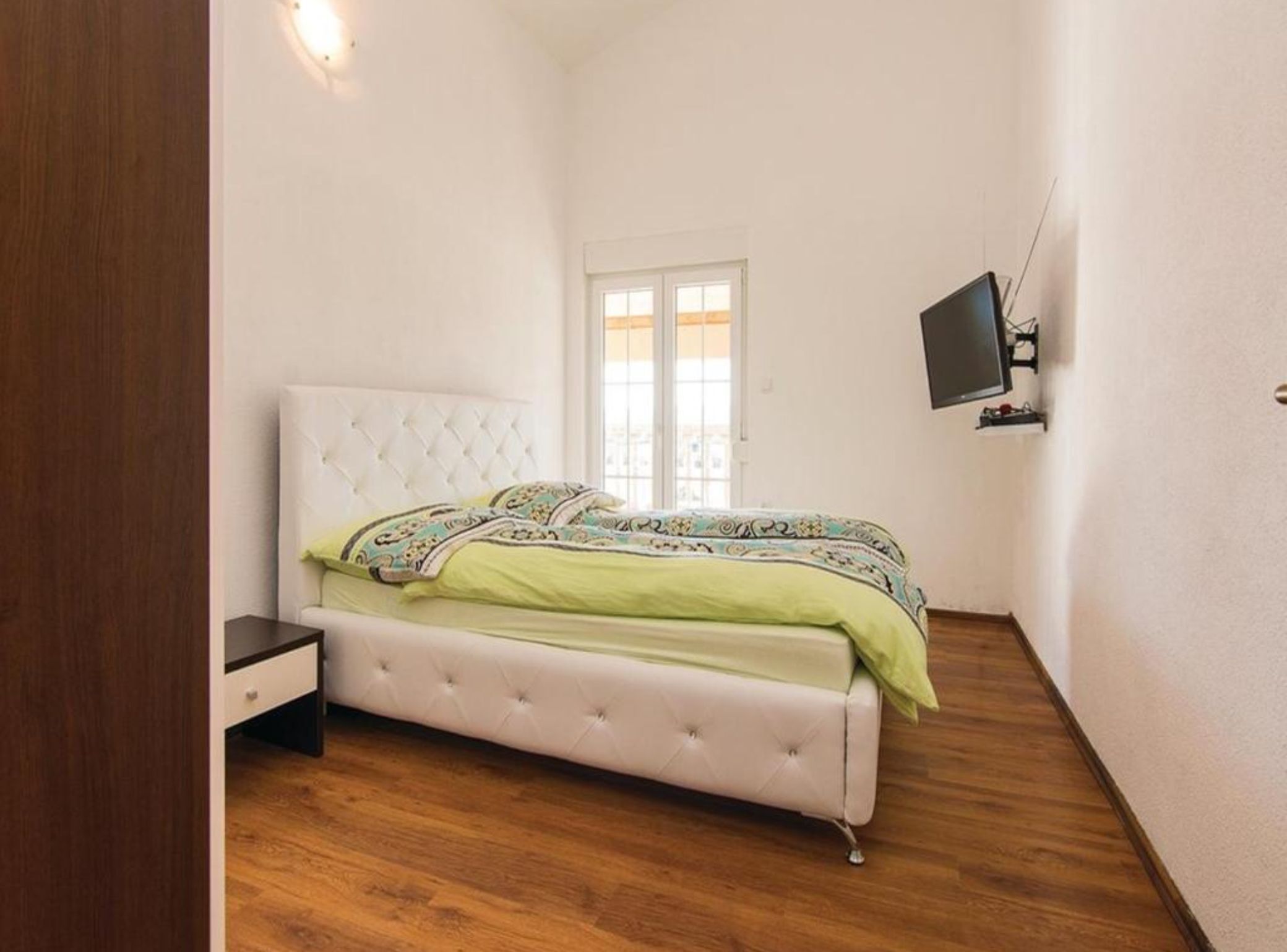 A bedroom with a bed, a nightstand, a television, and a window.