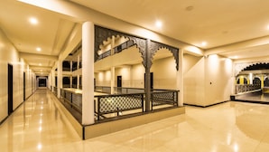 A spacious corridor with a central decorative archway, multiple doors, and a polished floor. - The Mewar Resort & Garden (Māvli)