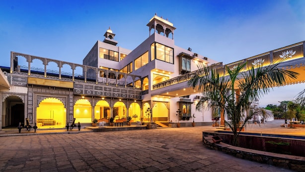 A multi-story building with a courtyard, featuring a balcony with railings, a staircase, and a series of arches. - The Mewar Resort & Garden (Māvli)