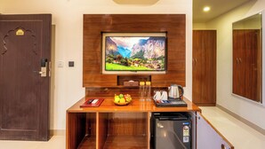 A hotel room with a wooden desk, a television mounted on the wall, a refrigerator, and a door labeled '101'. - The Mewar Resort & Garden (Māvli)