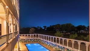 A courtyard with a swimming pool, surrounded by a decorative fence and a building with traditional architecture. - The Mewar Resort & Garden (Māvli)