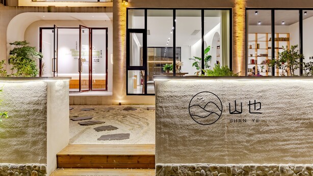 A modern hotel entrance with a glass door, a stone pathway, and a sign with the hotel's name.