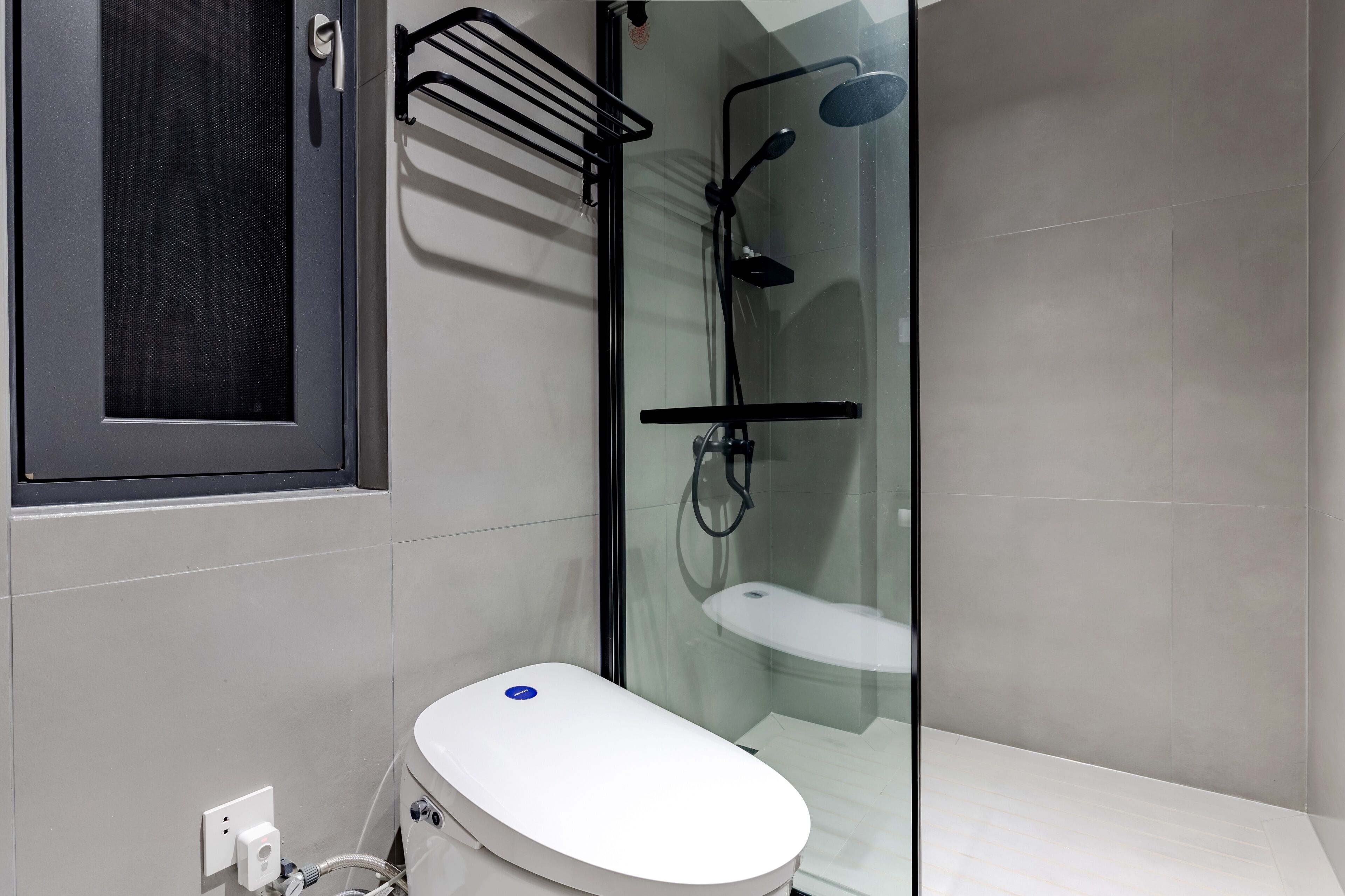 Une salle de bain moderne avec une douche à parois de verre, des toilettes blanches et un porte-serviettes noir.