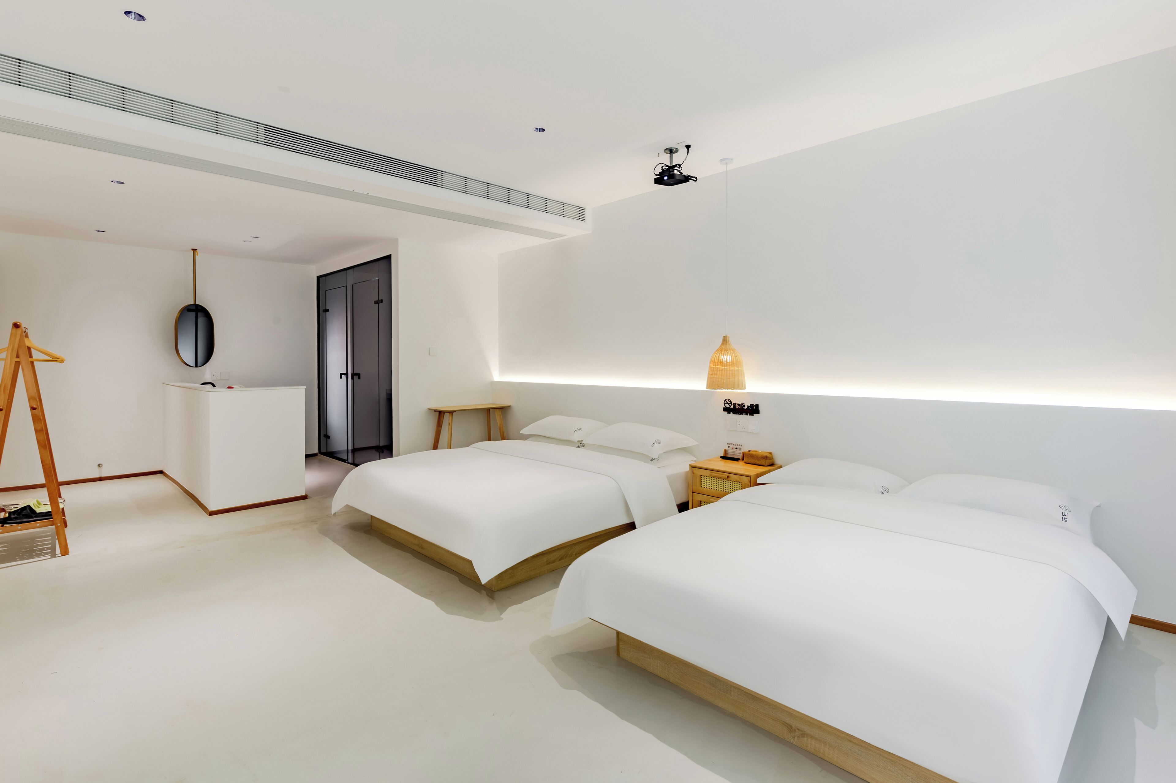A modern hotel room with two beds, a desk, a mirror, and a lamp.