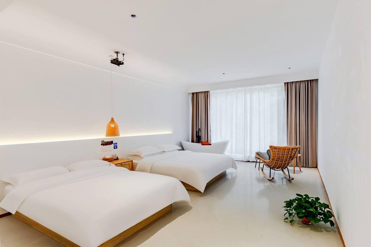 Una habitación de hotel moderna con dos camas, una zona de estar con una silla, una mesita pequeña y una planta en maceta.