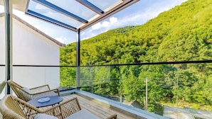 A balcony with wicker furniture and a glass railing overlooking a lush green hillside.
