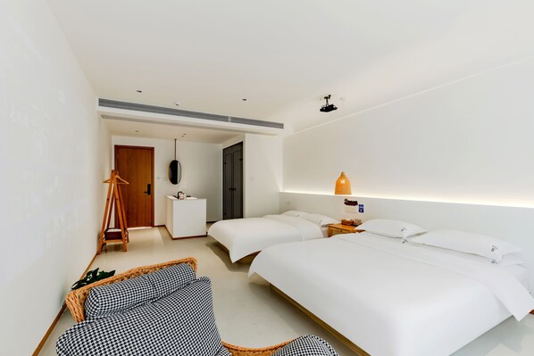 Una habitación de hotel moderna con una cama grande, dos mesitas de noche, una lámpara colgante y una zona de estar con un sofá estampado.