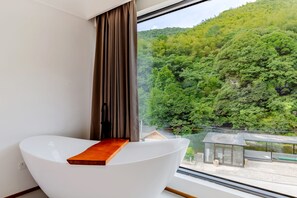 A modern bathroom with a white bathtub and a wooden tray. A large window offers a view of a forested hillside. - Shanye Guesthouse - Jingxian Shuimo Tingxi Scenic Area Branch (Xuancheng)