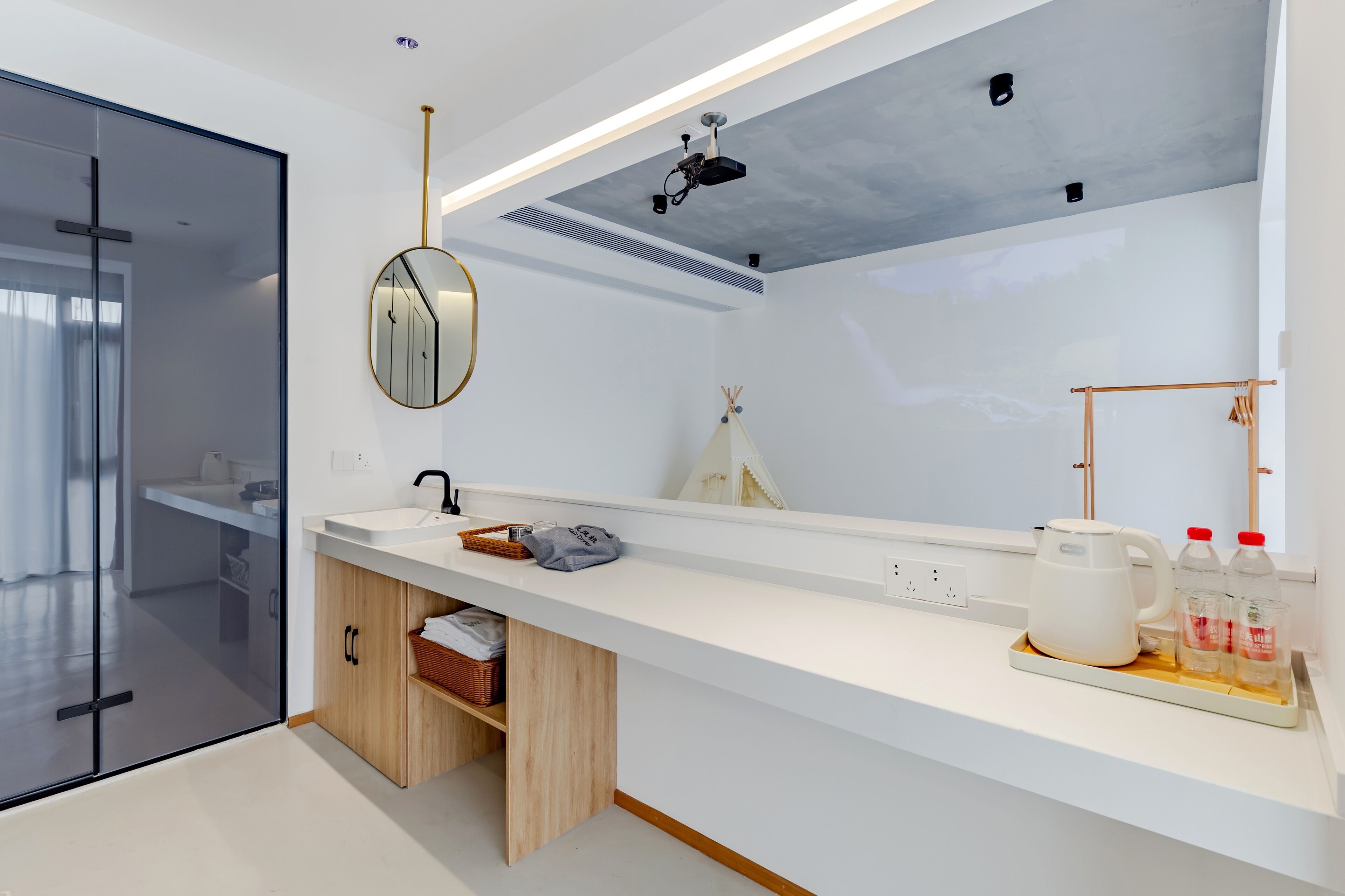 Un baño moderno con cabina de ducha de vidrio, encimera blanca, espejo, proyector en el techo y un perchero.