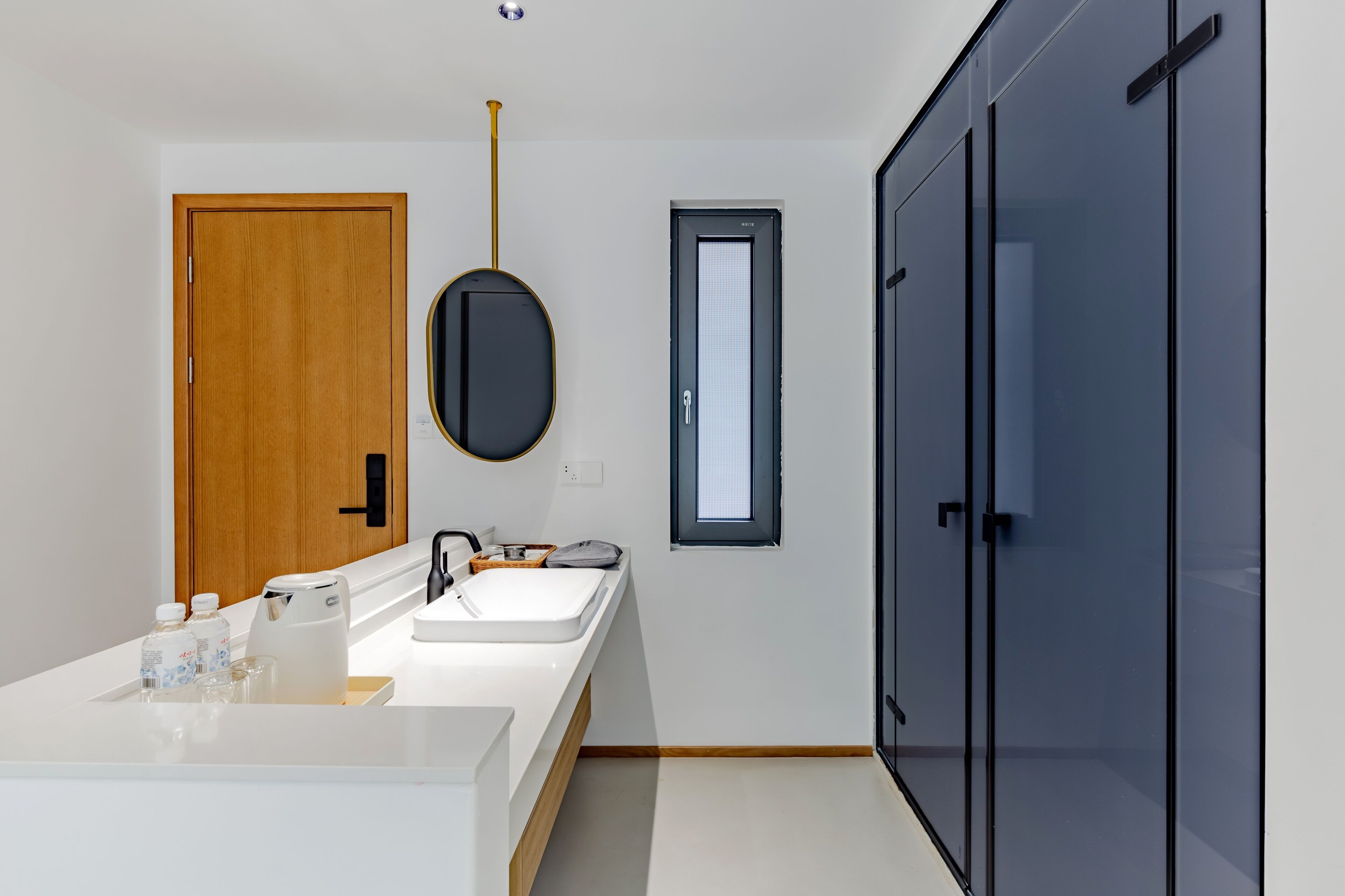 Un baño moderno con una puerta de madera, un lavabo blanco, un espejo y un armario negro.