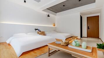 A modern hotel room with two beds, a wooden table with tea set, and a small plant.