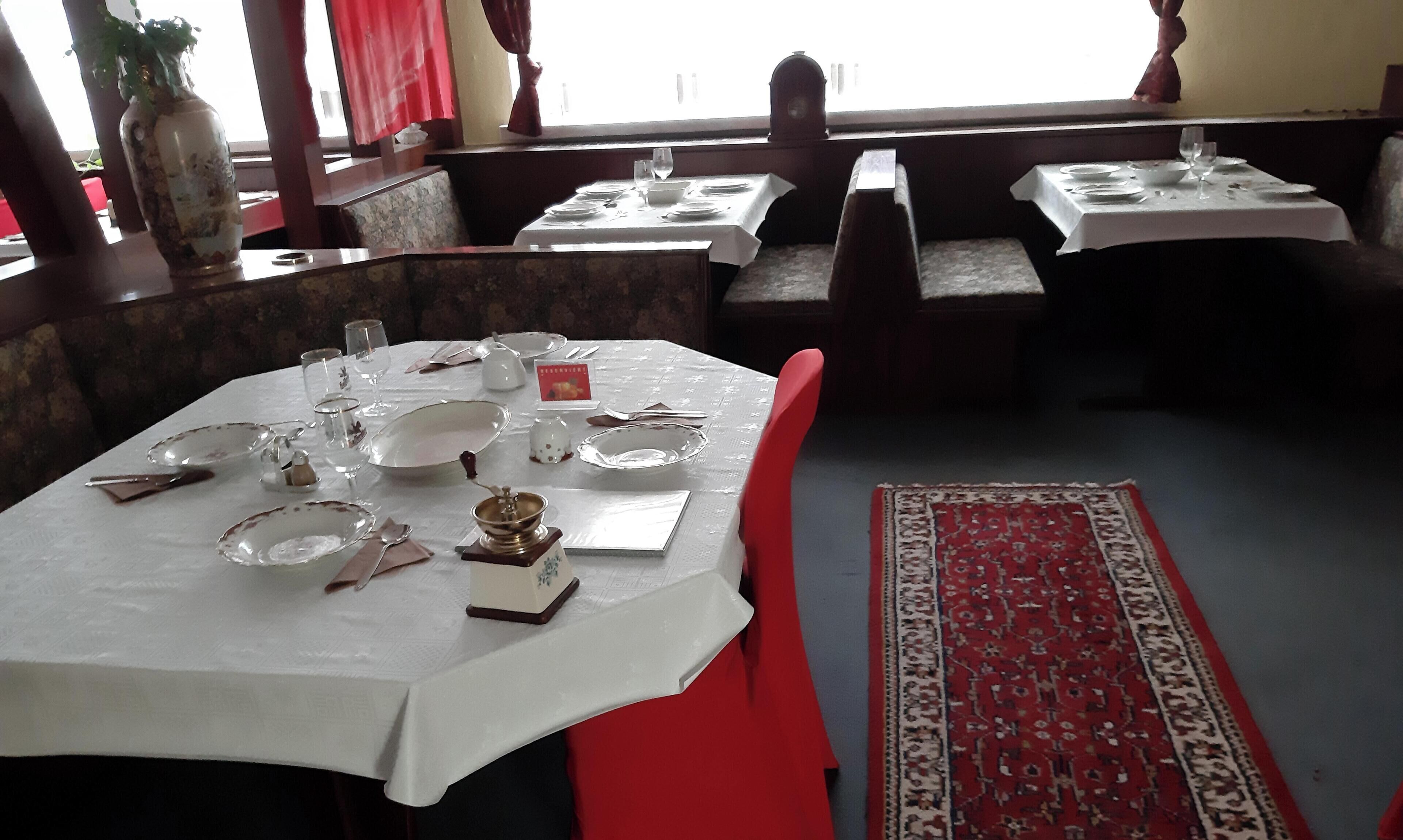 Ein Restaurant mit gedeckten Tischen, ausgestattet mit weißen Tischdecken und roten Stühlen.
