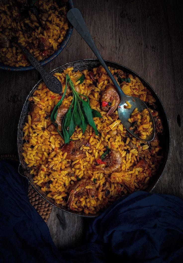A large pot of rice with meat and vegetables, a spoon, and a rustic wooden table.