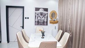 A dining area with a marble table, cushioned chairs, a framed artwork, a decorative mirror, and a door. - Tredview Hotel and Suites   (Lafia)