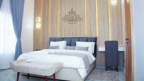 A modern bedroom with a bed, a bench, and a nightstand. - Tredview Hotel and Suites   (Lafia)