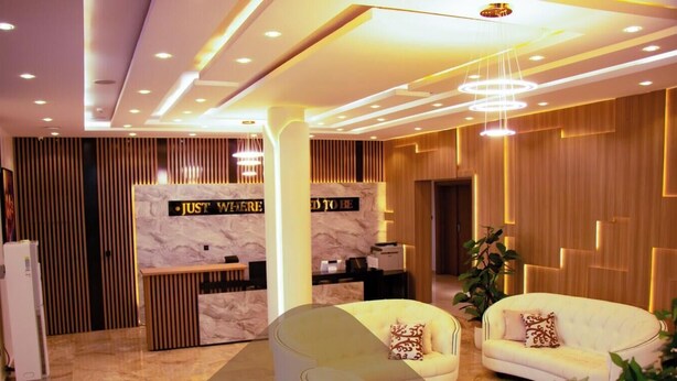 A modern reception area with a marble reception desk, two white sofas with patterned cushions, and a wooden panel wall. - Tredview Hotel and Suites   (Lafia)