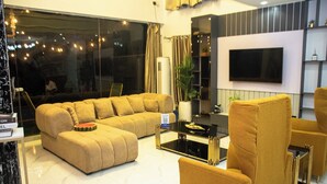 A modern living room with a sectional sofa, a coffee table, and a TV mounted on the wall. - Tredview Hotel and Suites   (Lafia)