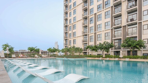 Piscina com espreguiçadeiras e um edifício alto ao fundo.
