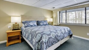 A bedroom with a large bed, two bedside tables with lamps, a nightstand, and a window with a view of trees. - All-Season Lake Wallenpaupack Condo w/ Views (Greentown)