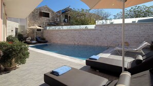 Una piscina con sillas de descanso y sombrillas, rodeada de muros de piedra y plantas en macetas.