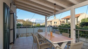 Un patio techado al aire libre con una mesa y sillas de mimbre, con vistas a una zona residencial.