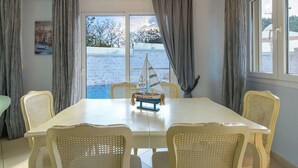 Un comedor con una mesa y sillas, una maqueta de un velero y vista al mar a través de amplios ventanales.