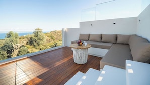A modern outdoor seating area with a wooden deck, a white round table, and a beige sofa with cushions. - Lofos Orizon Villa - Villa with pool in Crete (Mathés)