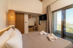 A bedroom with a bed, a desk, a TV, and a large window with a view of the landscape. - Lofos Orizon Villa - Villa with pool in Crete (Mathés)