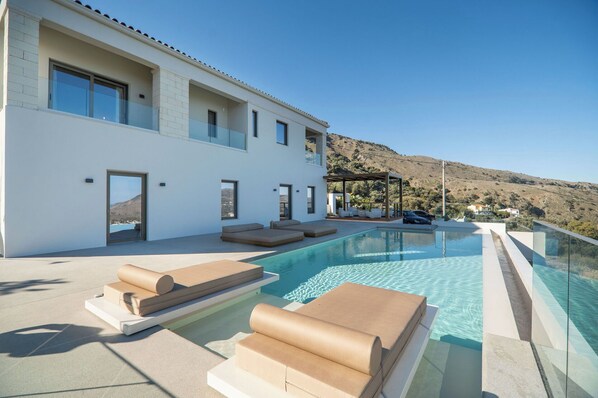 A modern house with a swimming pool, outdoor seating, and a view of the hills. - Lofos Orizon Villa - Villa with pool in Crete (Mathés)
