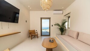 A modern living room with a flat-screen TV, a wooden coffee table, a wicker chair, a sofa, and a view of the ocean through a glass door. - Lofos Orizon Villa - Villa with pool in Crete (Mathés)