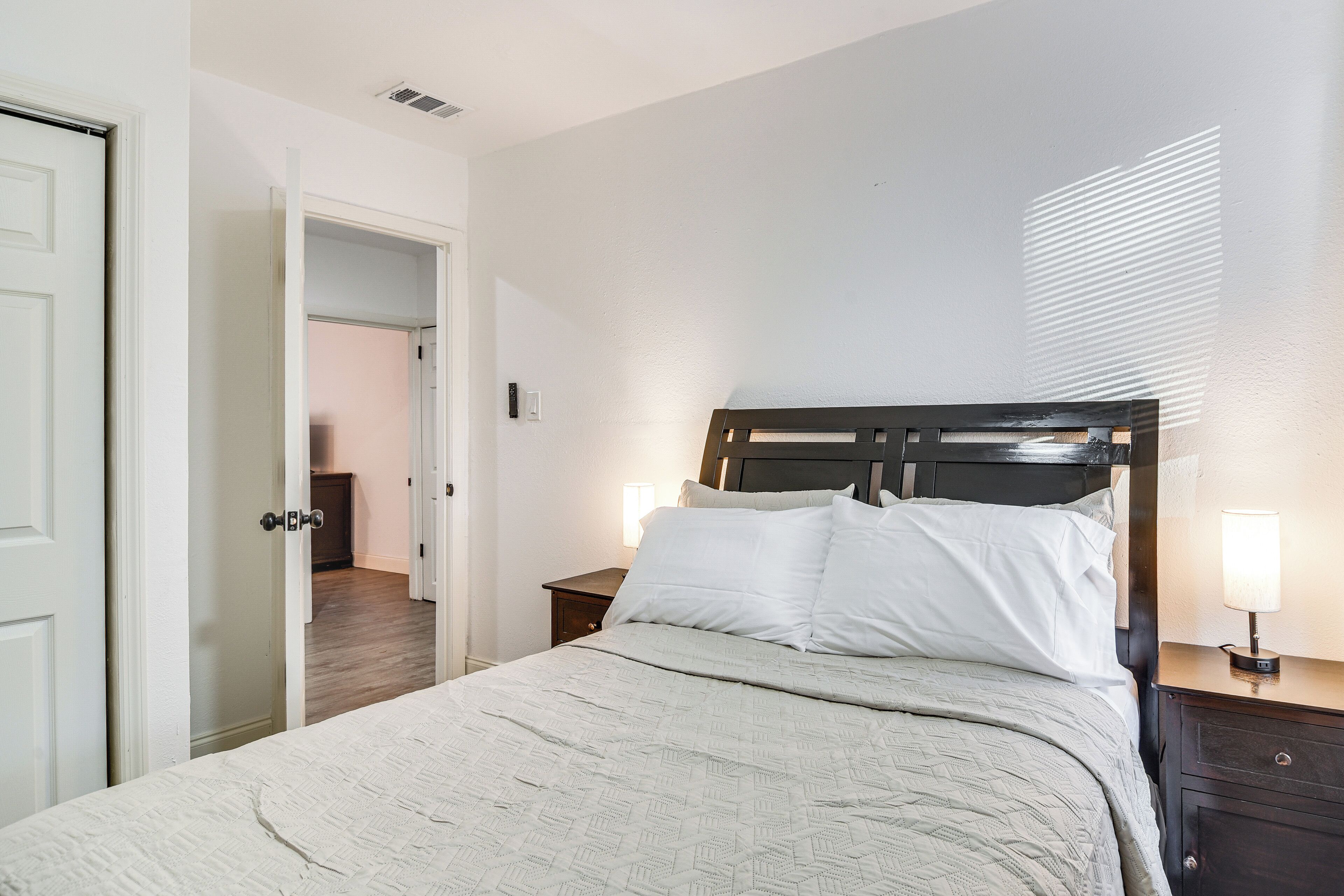 A bedroom with a bed, a nightstand, a lamp, and a door leading to another room.