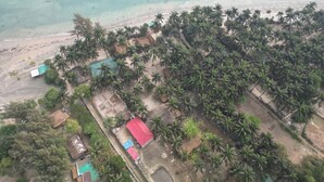 Eine Luftaufnahme einer Küstenlandschaft mit Strand, Palmen und kleinen Gebäuden mit roten Dächern.