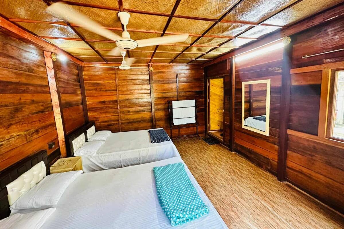 Ein Zimmer in einer Holzhütte mit zwei Betten, einem Deckenventilator und einem Fenster.