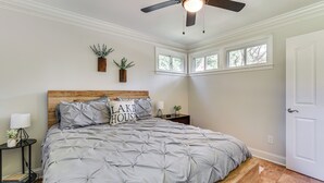Une chambre à coucher avec un lit, une table de chevet, une lampe, un ventilateur de plafond et une porte.