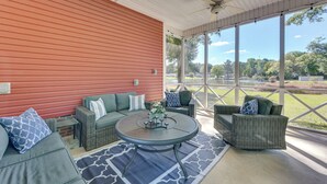 Une terrasse couverte, meublée de meubles en osier, avec une table ronde agrémentée d’un centre de table, et de grandes fenêtres offrant une vue sur l’extérieur.