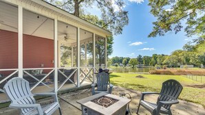 Une terrasse couverte avec des fauteuils Adirondack, un foyer et une vue sur un lac et un parc.