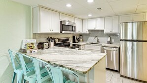 A modern kitchen with white cabinets, stainless steel appliances, and a marble countertop. - Walk to Shore + Restaurants: Resort Retreat in PCB (Panama City Beach)