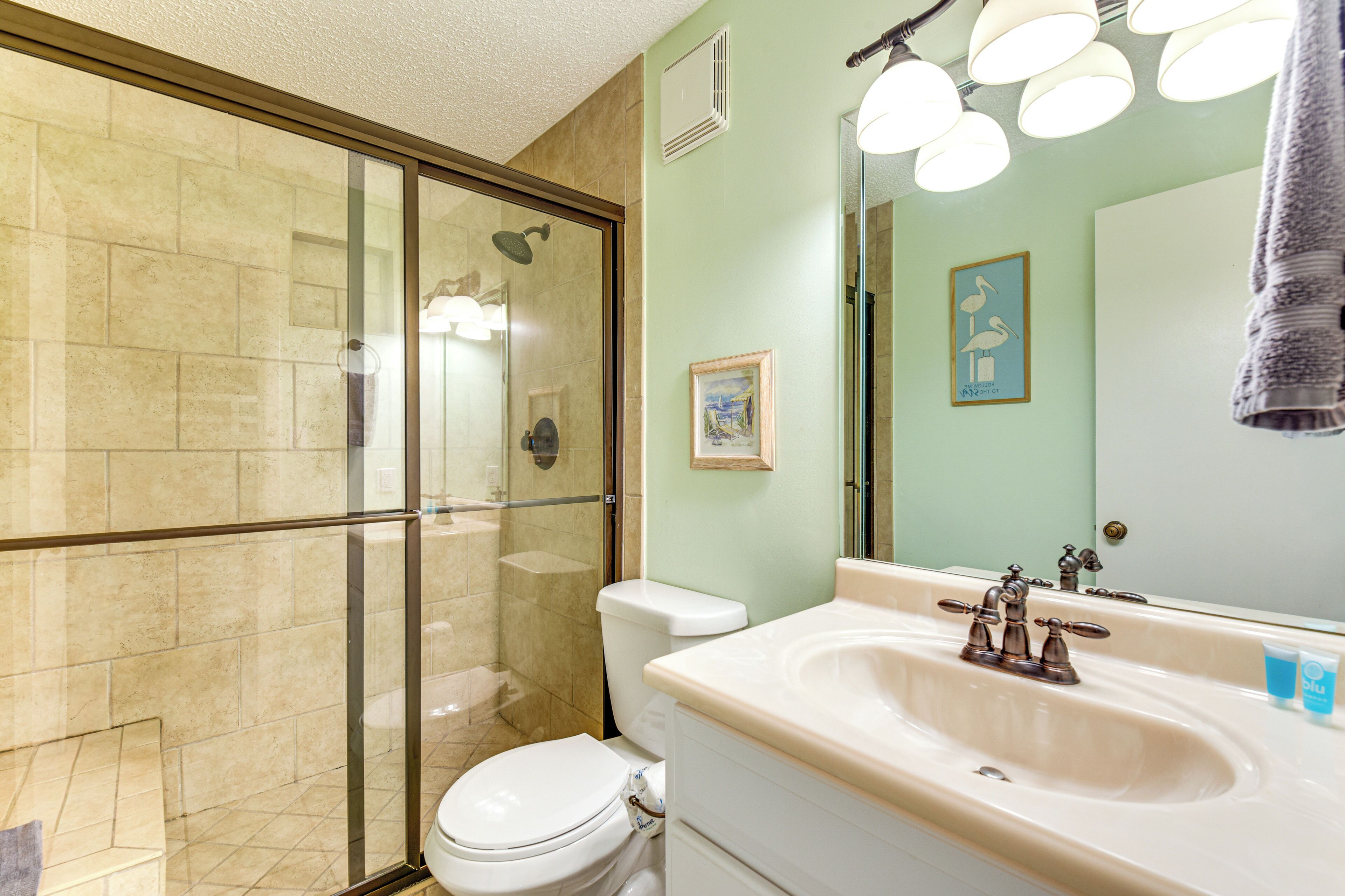 Une salle de bain avec une douche à parois de verre, des toilettes, un lavabo avec un miroir et un tableau encadré au mur.