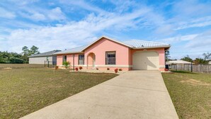 A single-story house with a pink facade, a garage, and a front yard with a concrete pathway.