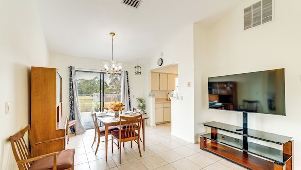 A spacious living area with a dining table, chairs, a TV, and a kitchen in the background.