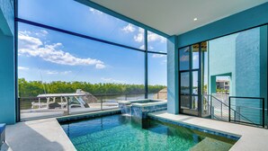 A modern indoor pool with clear water, large windows, and a view of a boat and greenery. - Luxury Group Escape in Cape Coral’s Cape Harbour! (Cape Coral)