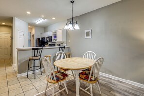 A kitchen with a dining area, white cabinets, a wooden table, and chairs with colorful cushions. - Steps to Pool & Golf! Condo 4 Mi to Myrtle Beach (Myrtle Beach)