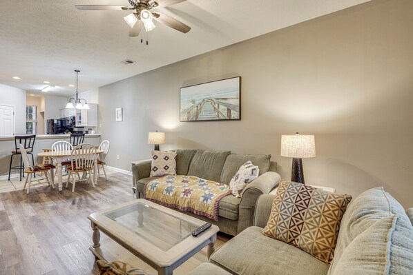A living room with a sofa, a coffee table, and a dining area with chairs and a table. - Steps to Pool & Golf! Condo 4 Mi to Myrtle Beach (Myrtle Beach)