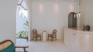 A modern interior with a round table and two chairs, a reception desk, and a large arched window. - Lumora Boutique Villas (Gili Trawangan)