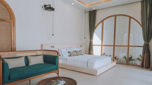 A modern bedroom with a bed, a green sofa, a round coffee table, and a large window with curtains. - Lumora Boutique Villas (Gili Trawangan)