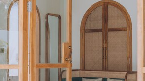 A room with a green sofa, a wicker chair, a large mirror, and a traditional wooden door. - Lumora Boutique Villas (Gili Trawangan)