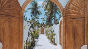 A pathway leading to a wooden door framed by arches, surrounded by tropical plants and palm trees. - Lumora Boutique Villas (Gili Trawangan)