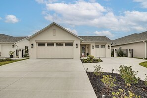 A modern two-story house with a garage, a driveway, and landscaped garden areas. - Beautiful Garden Villa with Golf Cart Option (Sumterville)