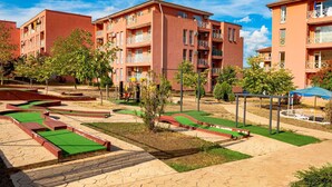Um pátio com edifícios vermelhos, grama sintética verde e um parquinho.