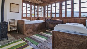 A rustic cabin with two wooden beds, a wooden dresser, and a large window overlooking a snowy landscape.
